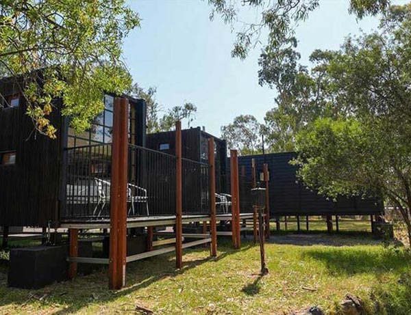 Elevated black-clad cabins nestled among trees at Stawell Grampians Gate C&C Park, blending modern design with a bushland setting.