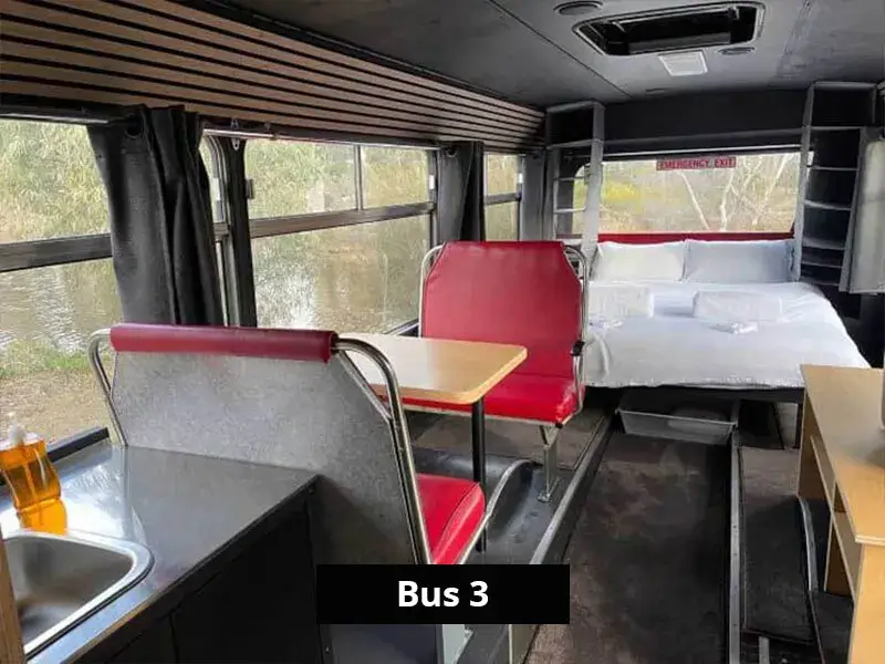 Retro-style red booth seating beside a kitchenette and a double bed at the back of Bus 3, overlooking the lake.