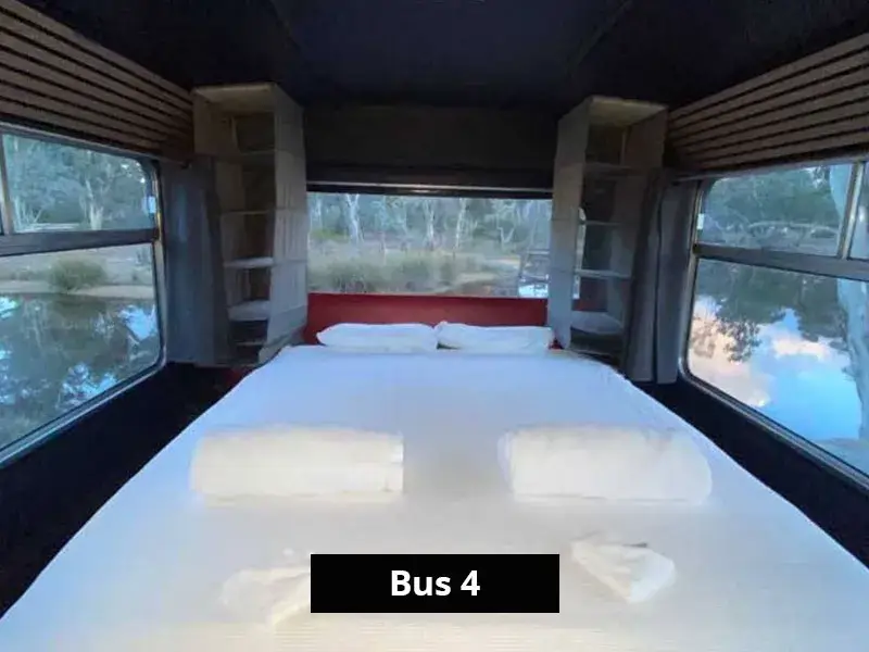 Spacious double bed setup at the back of Bus 4 with panoramic bushland and lake views through surrounding windows.
