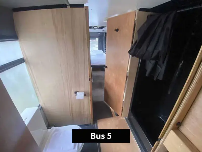 Compact bathroom area inside a converted bus accommodation with timber finishes, leading to the sleeping space at the rear.