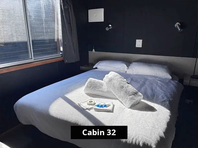 Main bedroom in Cabin 32 showcasing a neatly made queen bed with white linen, bedside lighting, and a large window letting in natural light.