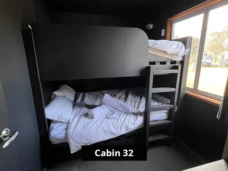 Cabin 32’s second bedroom featuring black-frame bunk beds, each with white bedding and pillows, positioned next to a large window for natural light.