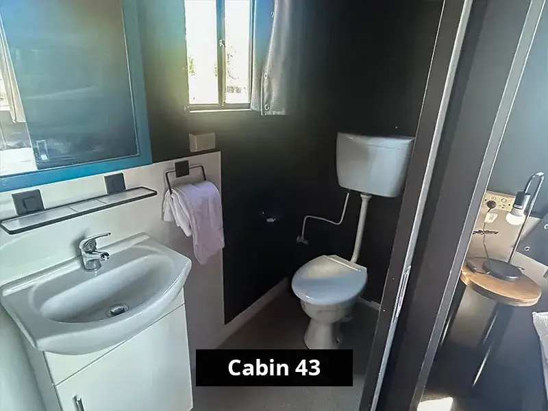 Ensuite bathroom inside Cabin 43 featuring a white vanity with integrated sink and chrome tapware, a mounted mirror, towel rail, and toilet beneath a frosted window, providing functional amenities in a private space.