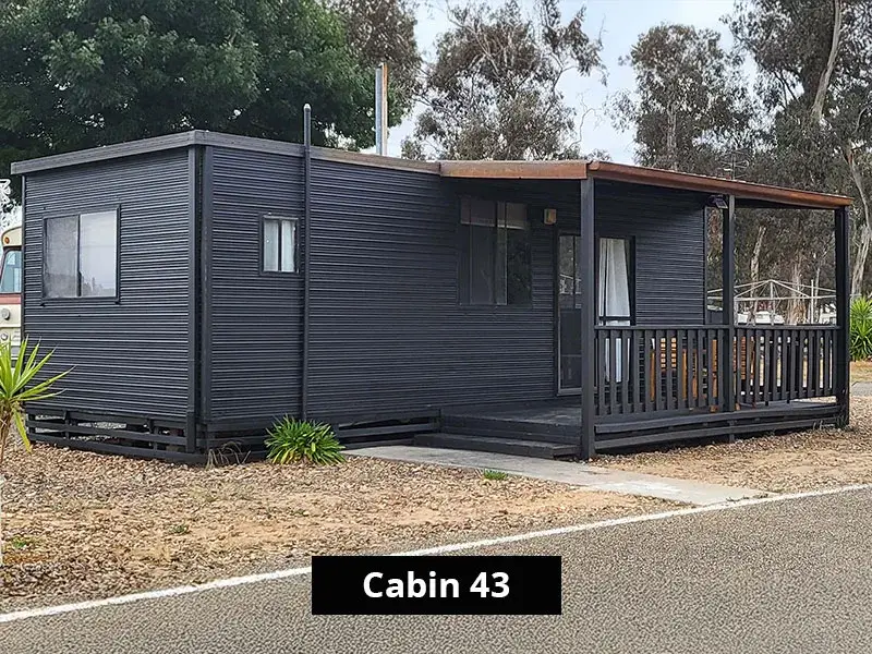 Exterior view of Cabin 43 at Grampians Gate Caravan Park in Stawell, showcasing a sleek black weatherboard design with a covered front deck, railing, and seating, ideal for relaxing outdoor stays.