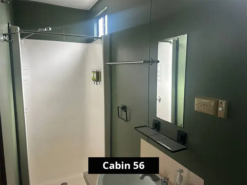 Modern bathroom inside Cabin 56 at Stawell C&C Park, featuring a large white shower cubicle, mounted toiletries, towel rack, mirror, and minimalist vanity sink against a green-toned wall.