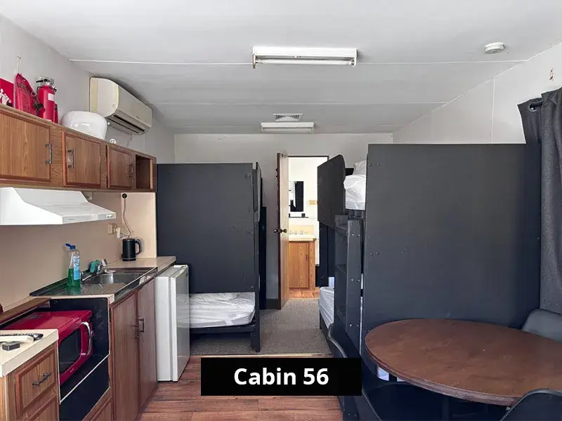 Interior of Cabin 56 at Grampians Gate caravan park, showcasing a shared space with two bunk beds, a compact kitchenette with wood cabinetry, red microwave, sink, and a round dining table.