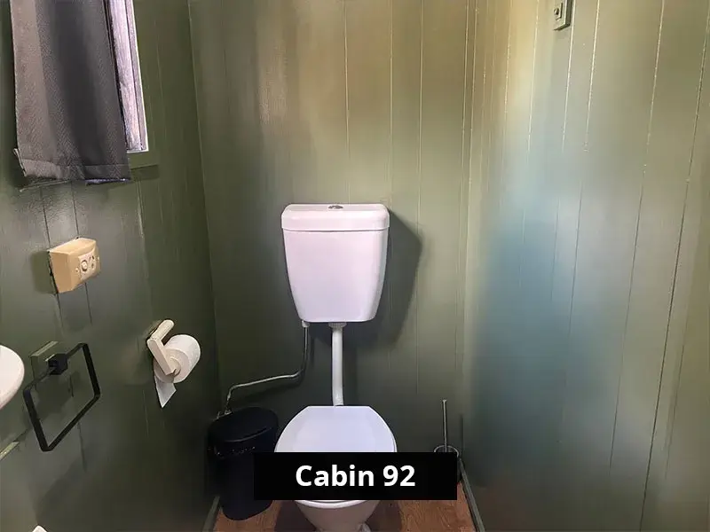 A private toilet inside Cabin 92 featuring olive green panelled walls, a high-set window for natural light, and essential amenities including a bin, toilet paper holder, and brush.