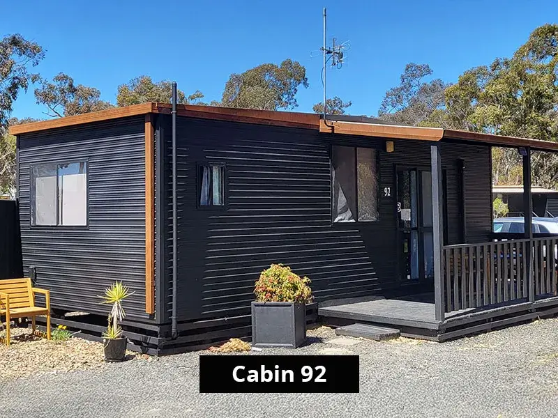 Modern black cabin exterior of Cabin 92 with timber accents, private deck and outdoor seating, located at Stawell C&C Park near the Grampians.