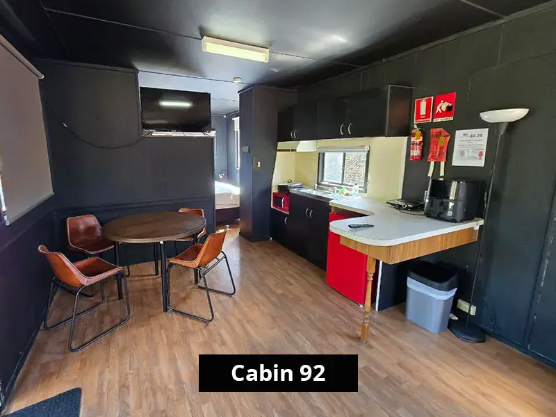 Self-contained Cabin 92 with open-plan kitchen, dining table, wall-mounted TV, and modern appliances at Grampians Gate Caravan Park in Stawell.