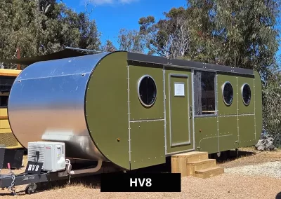 Modern green and silver HV8 caravan with circular windows and timber steps, set in a bushland environment at Stawell C&C Park near the Grampians.