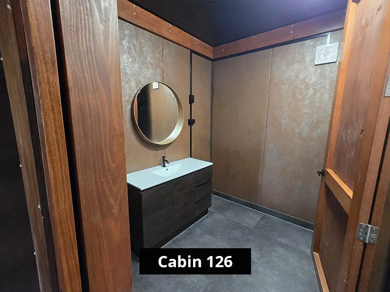 Modern cabin bathroom with round mirror, sleek vanity sink, and wood-paneled walls in minimalist style – Cabin 126