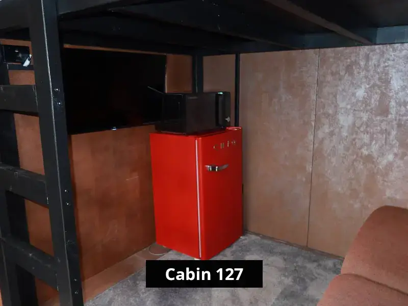 Cabin 127 interior corner with red mini fridge, microwave, bunk bed frame, and compact living space design.