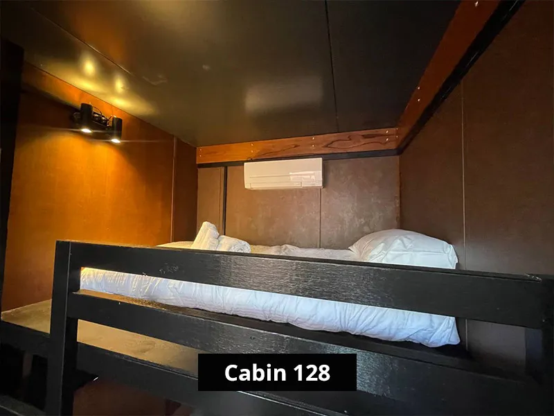 Close-up of upper bunk bed in cabin interior with wooden walls, reading light, and minimalist sleeping space.