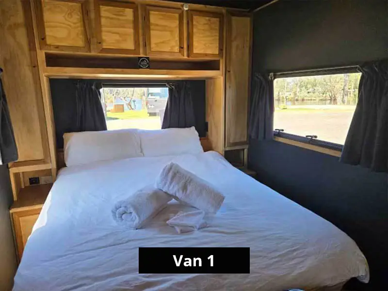 Van interior with double bed, overhead storage cabinets, bedside shelving and window views