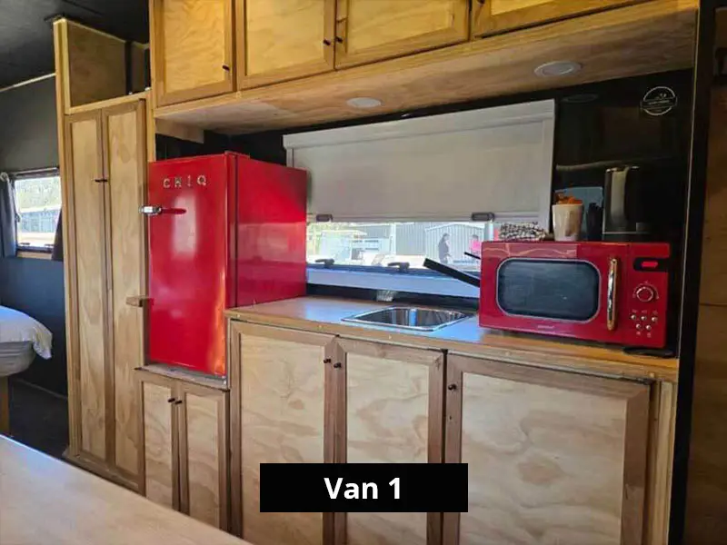 Van kitchenette with sink, red fridge, microwave, storage cabinets and window splashback