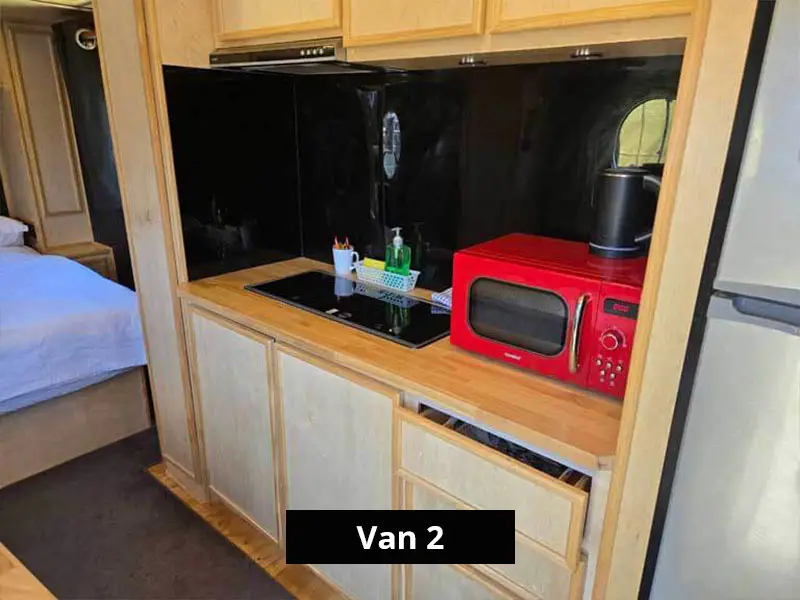 Van kitchenette with cooktop, red microwave, timber cabinetry and black splashback