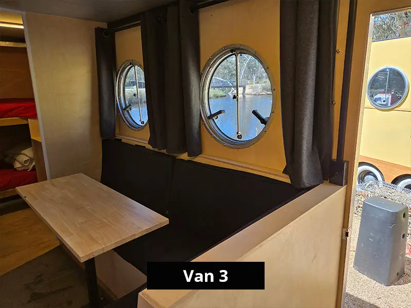 Van dining area with bench seating, timber table and round windows with outdoor view