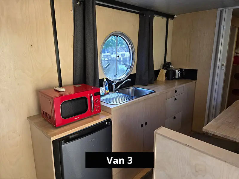 Van kitchenette with sink, microwave, mini fridge, storage cabinets and round window
