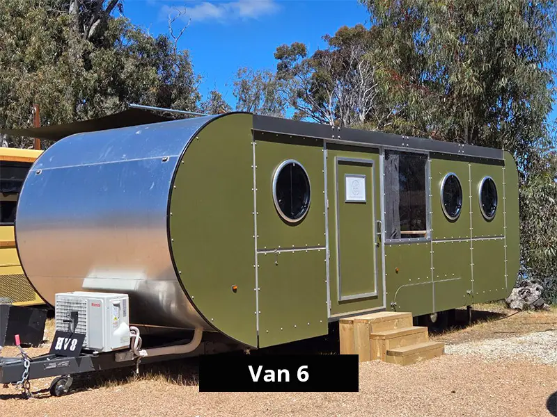 Modern caravan exterior with curved aluminium front, green paneling, round windows and entry steps