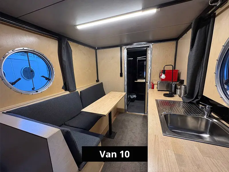 Small camper van interior with bench seating, dining table, kitchenette sink, and round windows in a modern tiny living space – Van 10