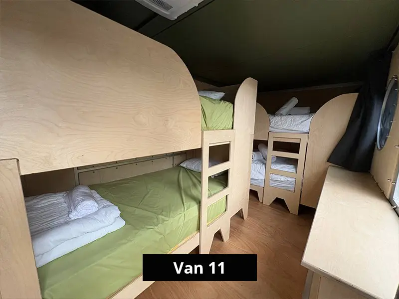 Small camper van bunk bed layout with wooden frames, green and white bedding, and compact sleeping quarters for group travel