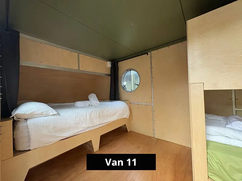 Minimalist camper van bedroom with single bed, wooden interior, and circular window, ideal for cozy off-grid living