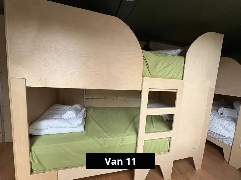 Close-up of wooden bunk beds inside camper van with green bedding, compact space-saving sleeping arrangement for road trips
