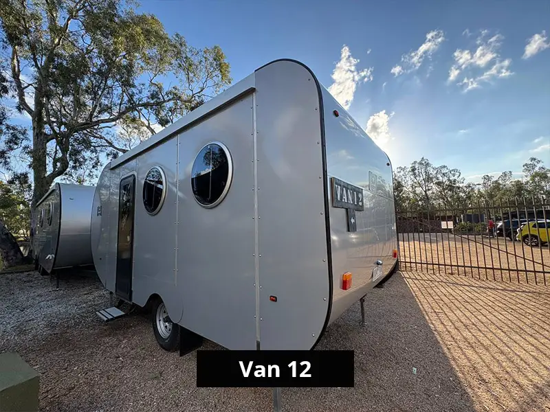 Rear angle view of Van 12 camper trailer with sleek gray exterior, round windows, and off-grid travel design in outdoor campsite