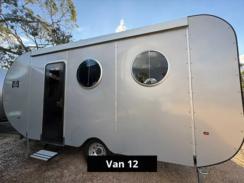 Modern compact retro van exterior Van 12 with round porthole windows and side entry door, parked outdoors in nature setting