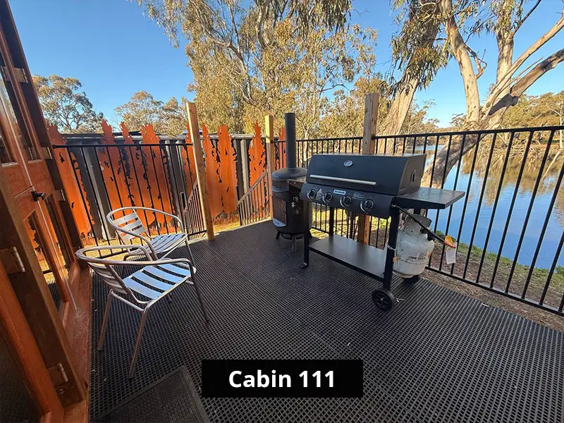 Private Cabin 111 lake front deck with barbecue grill, outdoor chairs, black railing, privacy screen, and eucalyptus tree views.