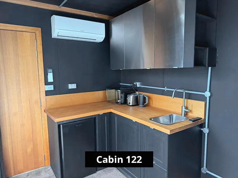 Cabin 122 kitchenette with black cabinets, timber benchtop, sink, mini fridge, microwave, kettle, toaster, and air conditioning.