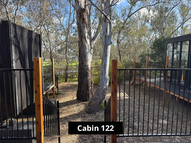 Cabin 122 exterior walkway with black railings, timber posts, modern cabin buildings, and surrounding eucalyptus bushland.